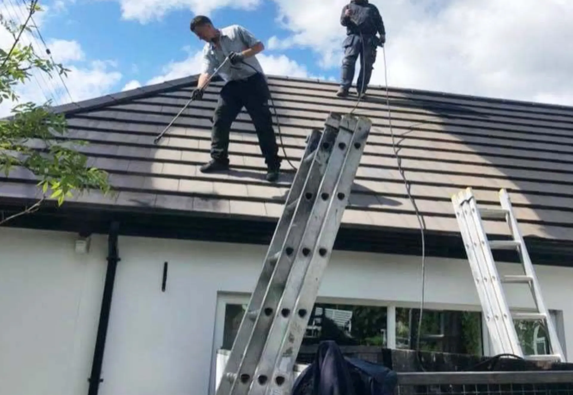 Two technicians treating a tiled roof with low pressure spray lances