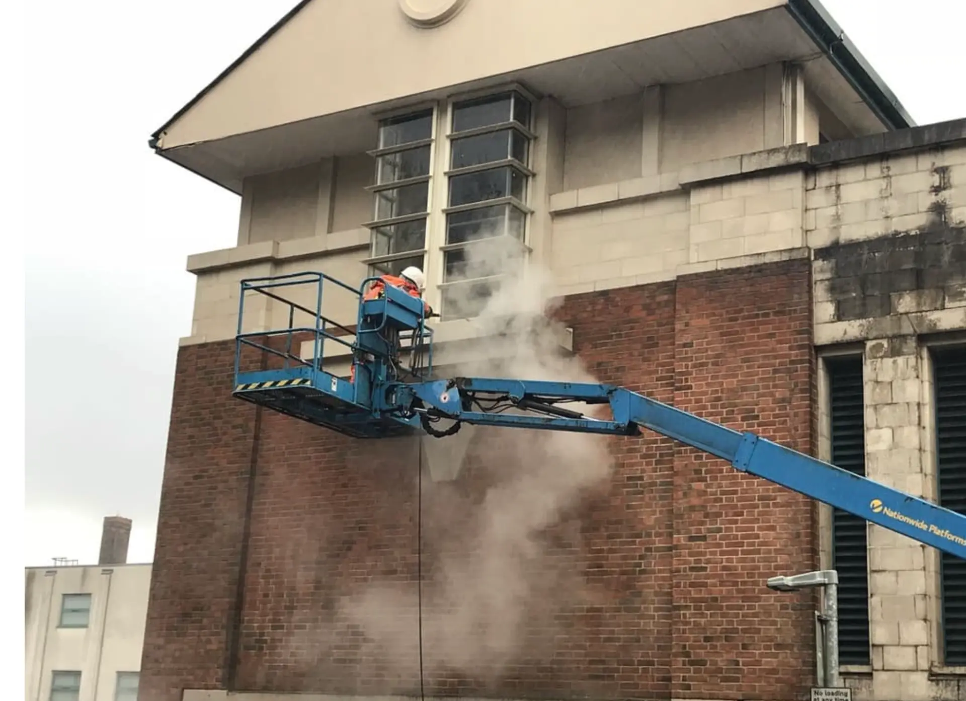 Operator steam cleaning a brick building from a boom lift platform