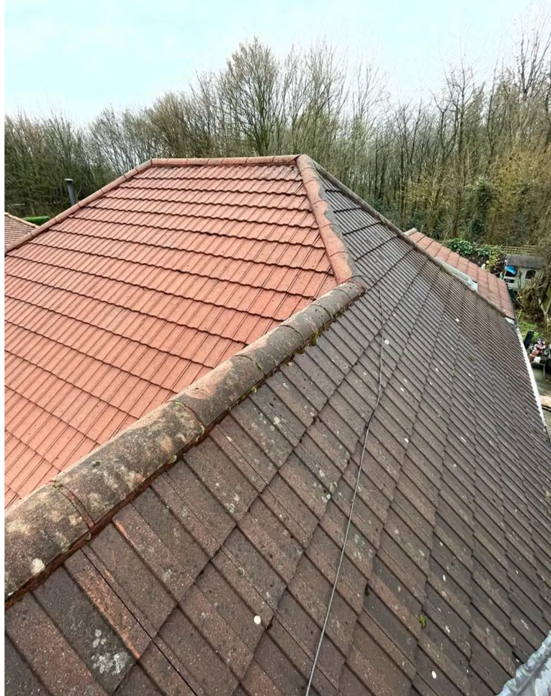 Roof ridge with one side cleaned to bright terracotta and the other still dark